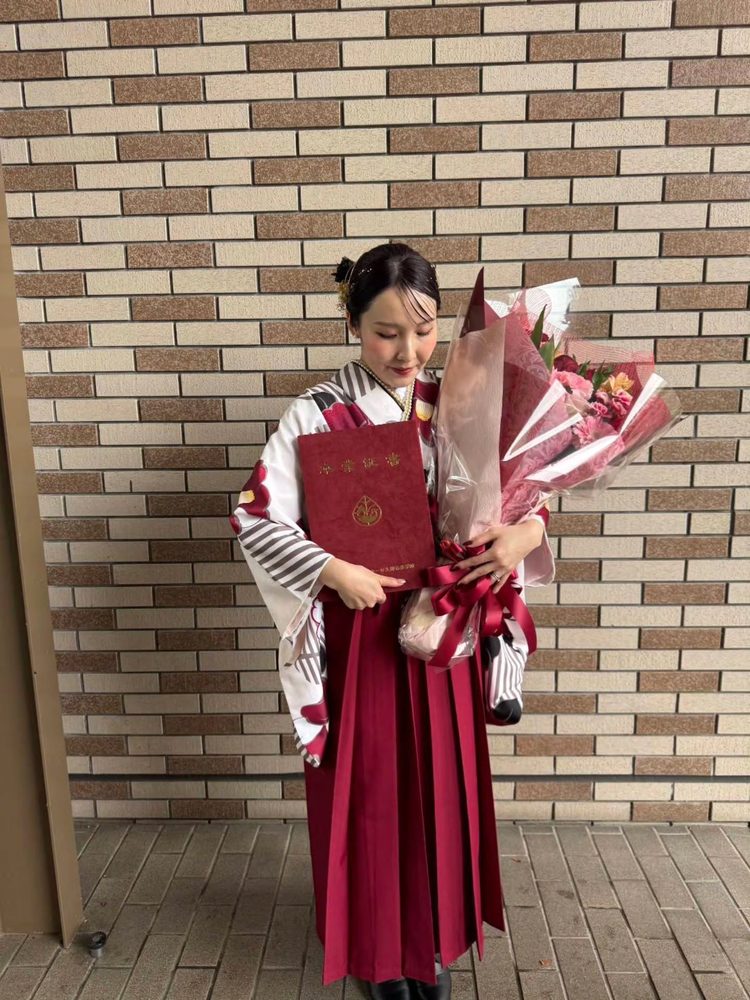 白地の二尺袖にえんじの袴で花束を持つお客様（卒業式）